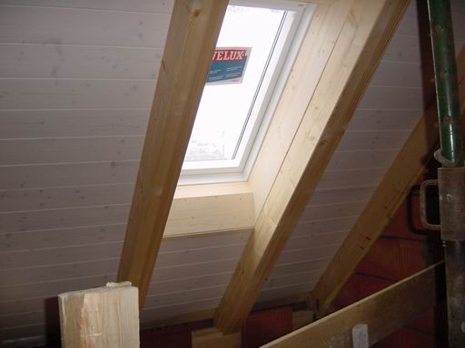 Dachflächenfenster zwischen sichtbaren Holzbalken im Dachgeschoss
